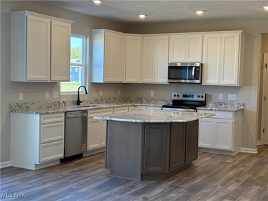 Kitchen featuring white cabinets, appliances with stainless steel finishes, light stone counters, a textured ceiling, and dark wood finished floors