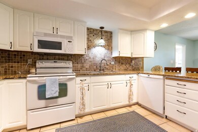 Kitchen featuring white appliances, white cabinetry, dark stone counters, light tile patterned floors, and recessed lighting