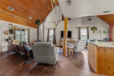 Living room with a wood stove, high vaulted ceiling, concrete floors, plenty of natural light, and wood ceiling