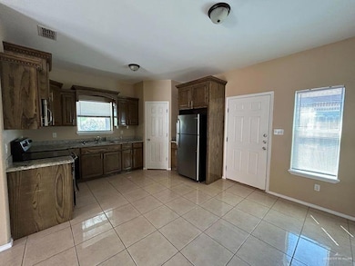 Kitchen featuring appliances with stainless steel finishes, light tile patterned flooring, light stone counters, and dark brown cabinets