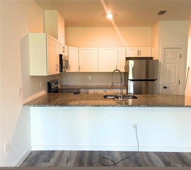 Kitchen with appliances with stainless steel finishes, a sink, dark stone counters, dark wood-style flooring, and a peninsula