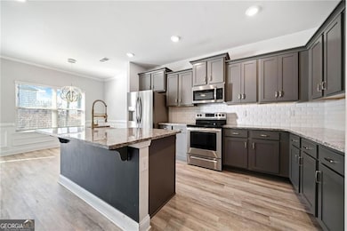 Kitchen featuring a center island with sink, appliances with stainless steel finishes, a breakfast bar, light stone countertops, and a sink