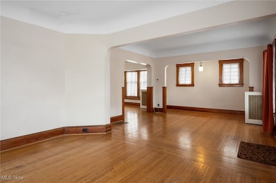 Spare room with hardwood / wood-style floors, arched walkways, and radiator