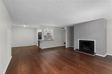 Unfurnished living room featuring dark wood finished floors, baseboards, a textured ceiling, and a fireplace with raised hearth