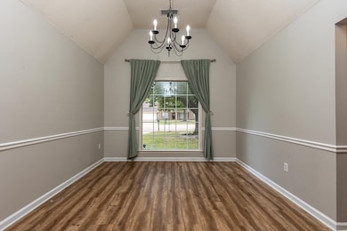 Empty room with a chandelier, dark wood finished floors, lofted ceiling, and a textured ceiling