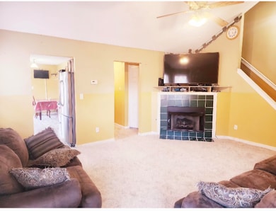Carpeted living room with ceiling fan and a firepl