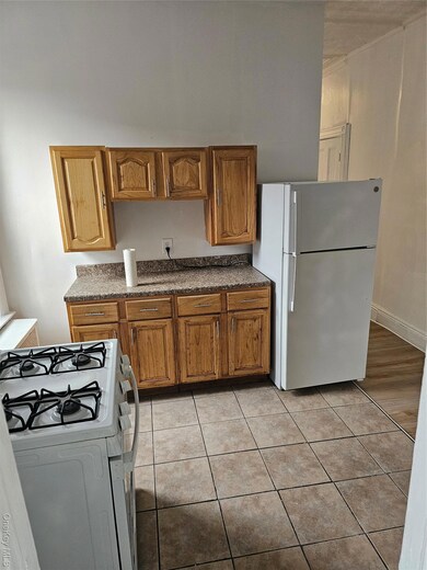 Kitchen with stove, brown cabinets, fridge, dark countertops, and light tile patterned floors