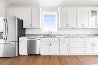 Kitchen with appliances with stainless steel finishes, a sink, white cabinets, light stone countertops, and ornamental molding
