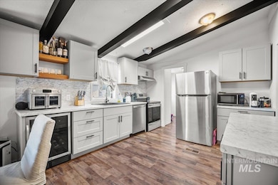 Kitchen with appliances with stainless steel finishes, tasteful backsplash, wood finished floors, and white cabinets