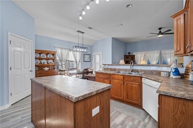 Kitchen featuring brown cabinetry, hanging light fixtures, a textured ceiling, white dishwasher, and lofted ceiling