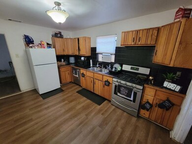 Kitchen with stainless steel appliances, dark countertops, dark wood-style floors, and brown cabinetry