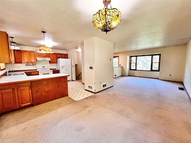 Kitchen featuring brown cabinets, pendant lighting, light countertops, a peninsula, and a textured ceiling