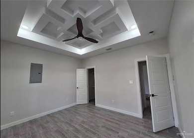 Unfurnished bedroom with coffered ceiling, electric panel, light wood-style floors, a walk in closet, and ceiling fan