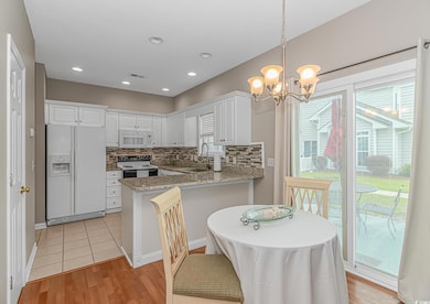 Kitchen featuring white appliances, a sink, a peninsula, tasteful backsplash, and white cabinetry