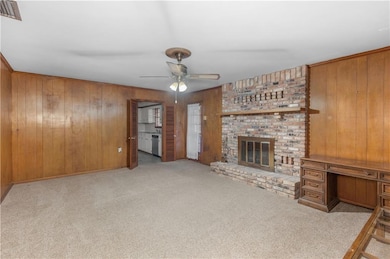 Unfurnished living room with wood walls, carpet floors, a brick fireplace, a ceiling fan, and a desk