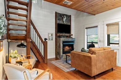 Living area featuring light wood-style floors, wood ceiling, stairs, a stone fireplace, and wooden walls
