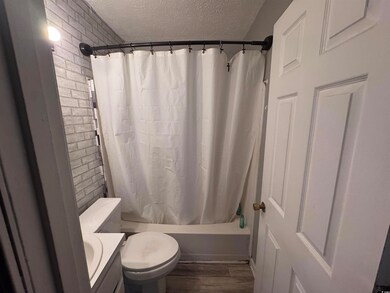 Full bath featuring a textured ceiling, brick wall, toilet, shower / tub combo with curtain, and wood finished floors