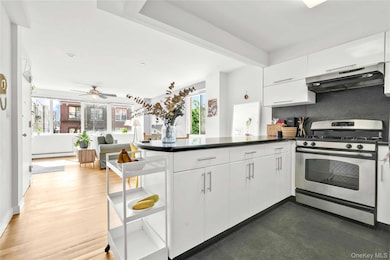 Kitchen with stainless steel gas stove, a peninsula, white cabinets, ventilation hood, and tasteful backsplash