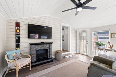 Living room with vaulted ceiling, wood finished floors, a fireplace, wooden walls, and ceiling fan