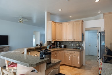 Kitchen with light brown cabinets, tasteful backsplash, freestanding refrigerator, recessed lighting, and a peninsula