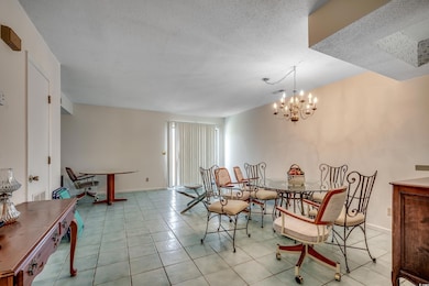 Tiled dining room with a textured ceiling, a chandelier, and baseboards