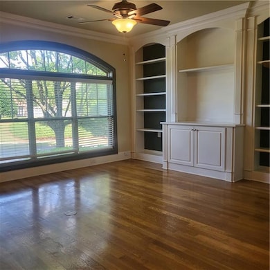 Unfurnished room with built in features, crown molding, a ceiling fan, and dark wood finished floors