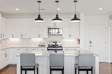 Kitchen with a kitchen breakfast bar, dark wood-style flooring, pendant lighting, white cabinetry, and recessed lighting