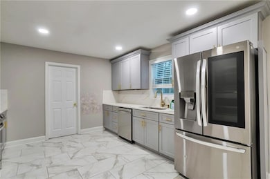 Kitchen featuring appliances with stainless steel finishes, gray cabinets, light marble finish flooring, recessed lighting, and light stone countertops