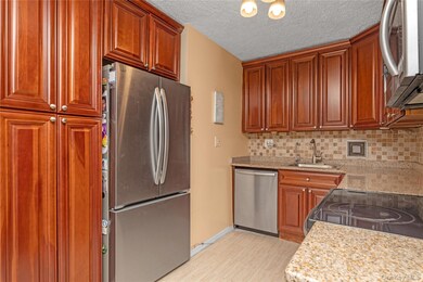Kitchen with appliances with stainless steel finishes, light stone counters, backsplash, brown cabinets, and a textured ceiling