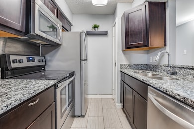 Kitchen with appliances with stainless steel finishes, light stone counters, dark brown cabinets, and a textured ceiling