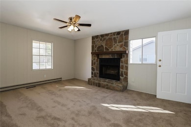 Unfurnished living room featuring wood walls, a baseboard radiator, a stone fireplace, carpet floors, and a ceiling fan