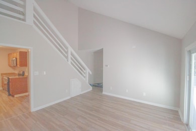 Unfurnished living room featuring stairs, light wood-style flooring, lofted ceiling, and baseboards