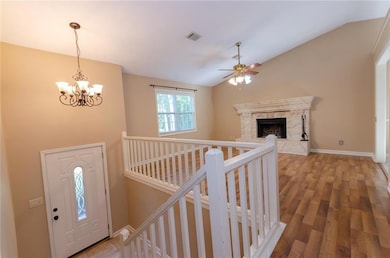 Foyer entrance featuring a high end fireplace, a chandelier, hardwood flooring, a ceiling fan, and vaulted ceiling