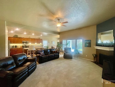 Living area featuring ceiling fan, light colored carpet, a fireplace with flush hearth, and a textured ceiling