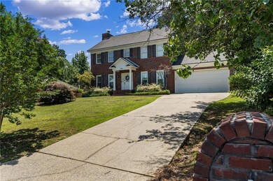 Colonial-style house featuring brick siding, a chimney, a front lawn, and concrete driveway