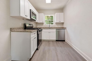 Kitchen featuring appliances with stainless steel finishes, light wood finished floors, white cabinetry, and light stone counters