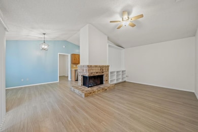 Unfurnished living room featuring lofted ceiling, light wood finished floors, a textured ceiling, a fireplace, and a chandelier