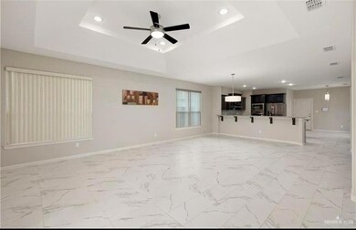 Unfurnished living room with a tray ceiling, ceiling fan, and light tile floors
