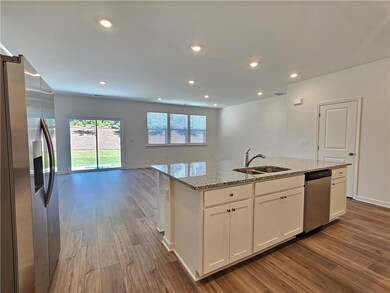 Kitchen with appliances with stainless steel finishes, wood finished floors, light stone countertops, an island with sink, and recessed lighting