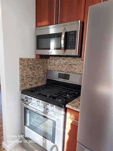 Kitchen featuring stainless steel appliances, brown cabinets, light stone counters, and tasteful backsplash