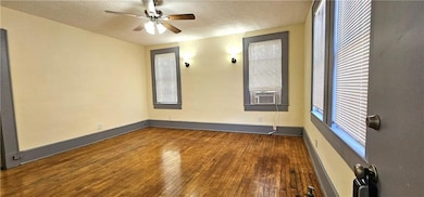 Empty room featuring hardwood / wood-style flooring, a ceiling fan, a textured ceiling, baseboards, and cooling unit