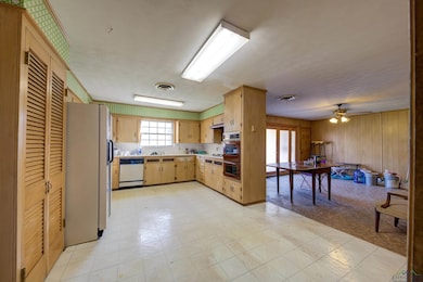 Kitchen with light flooring, white appliances, light countertops, light brown cabinets, and a ceiling fan