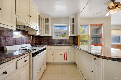 Kitchen with white gas range, dark stone counters, decorative backsplash, under cabinet range hood, and cream cabinets