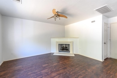 Unfurnished living room featuring dark wood-style flooring, a ceiling fan, and a fireplace with raised hearth