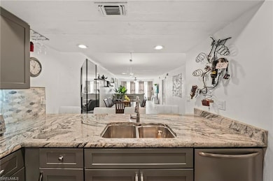 Kitchen with gray cabinetry, visible vents, light stone countertops, and a sink