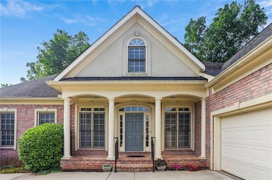 View of exterior entry featuring brick siding, a shingled roof, stucco siding, a garage, and covered porch