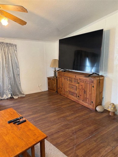 Unfurnished living room featuring a textured ceiling, a textured wall, dark wood-style flooring, and ceiling fan