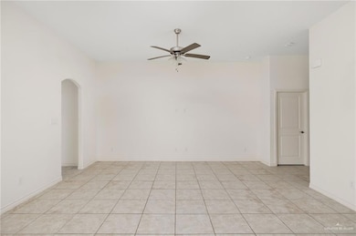 Empty room with arched walkways, light tile patterned flooring, and a ceiling fan