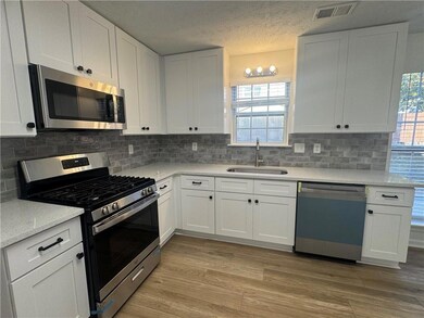 Kitchen with stainless steel appliances, white cabinets, light stone counters, light wood-style floors, and decorative backsplash