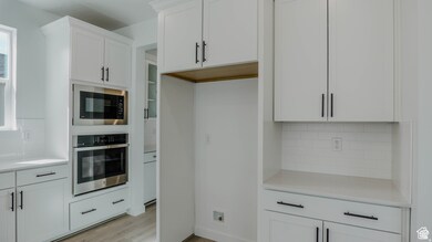 Kitchen featuring decorative backsplash, oven, white cabinetry, built in microwave, and light wood-style flooring
